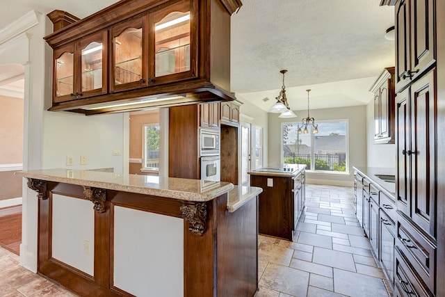 kitchen featuring oven, stainless steel microwave, a kitchen island, hanging light fixtures, and light stone counters