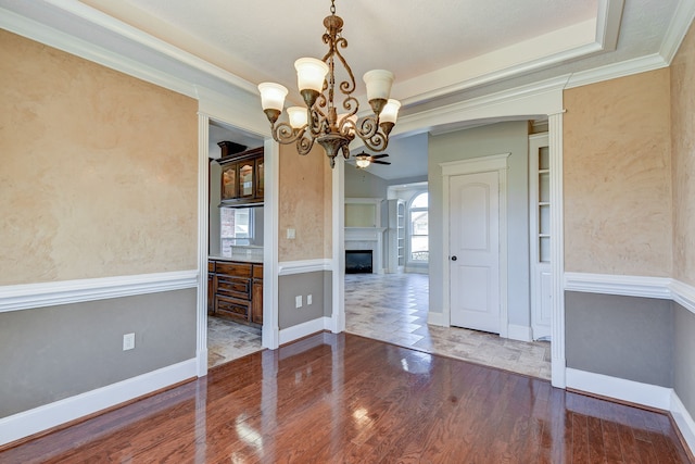 unfurnished dining area featuring crown molding, dark hardwood / wood-style flooring, and ceiling fan with notable chandelier