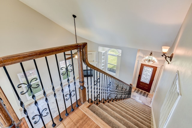 stairway featuring a notable chandelier, wood-type flooring, and lofted ceiling