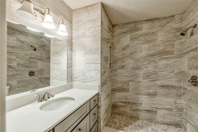 bathroom with tiled shower, vanity, and a textured ceiling