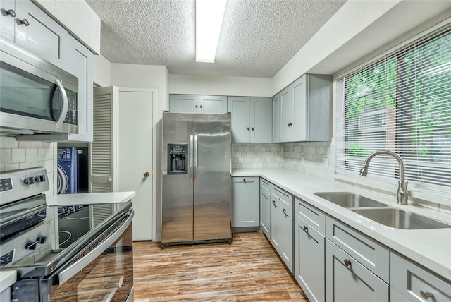 kitchen featuring appliances with stainless steel finishes, sink, light wood-type flooring, and decorative backsplash