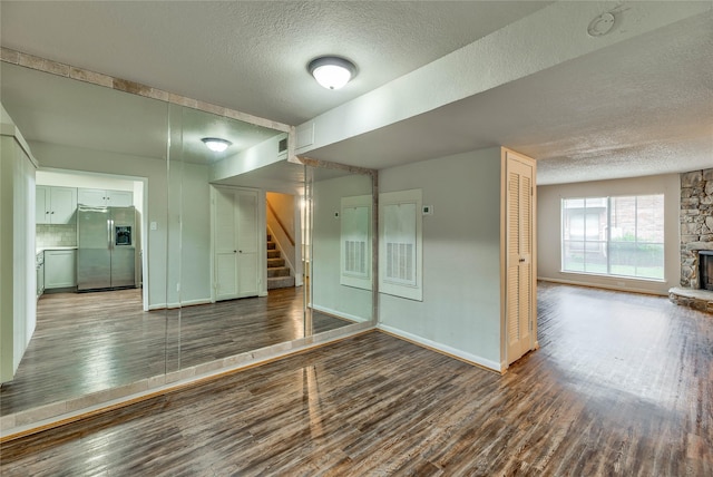 unfurnished room featuring hardwood / wood-style flooring, a stone fireplace, and a textured ceiling