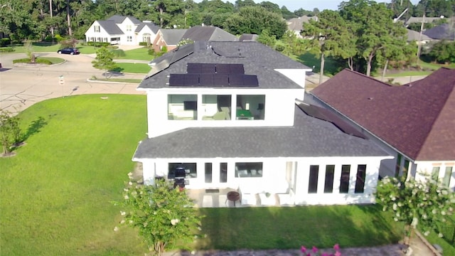 rear view of property featuring solar panels, a yard, a residential view, and roof with shingles