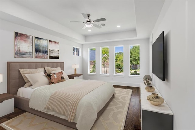 bedroom with dark hardwood / wood-style flooring, a raised ceiling, and ceiling fan