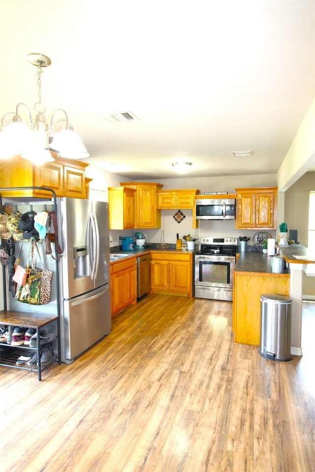 kitchen with sink, decorative light fixtures, light hardwood / wood-style floors, kitchen peninsula, and stainless steel appliances