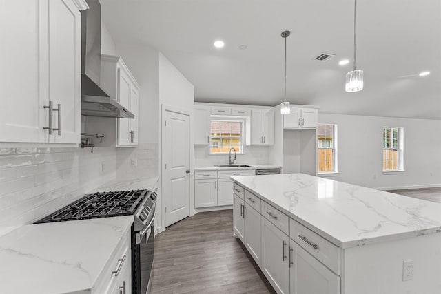 kitchen featuring stainless steel gas range oven, wall chimney range hood, decorative light fixtures, a kitchen island, and white cabinetry