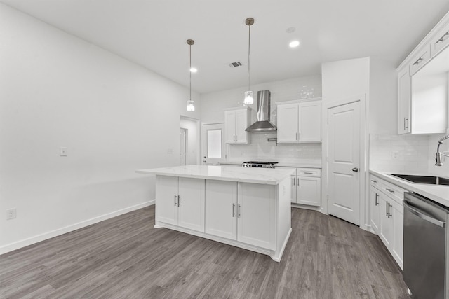 kitchen with hardwood / wood-style floors, wall chimney range hood, stainless steel dishwasher, a kitchen island, and white cabinetry