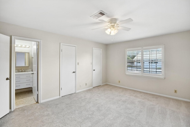 unfurnished bedroom featuring ensuite bathroom, ceiling fan, light colored carpet, and two closets