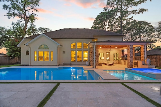 pool at dusk featuring a patio, an outdoor living space with a fireplace, fence, and a ceiling fan