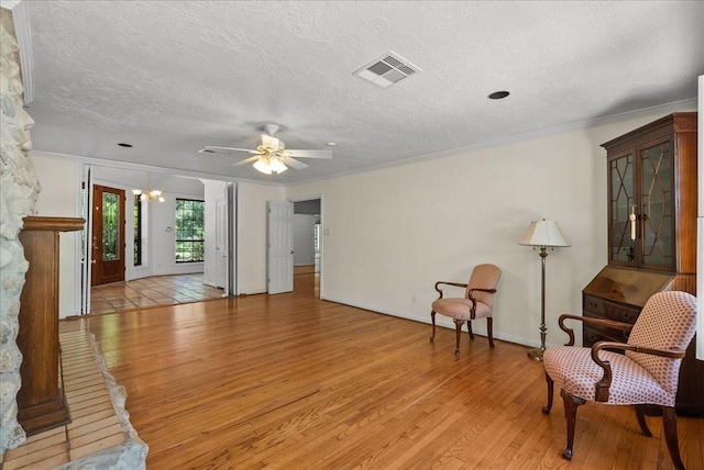 sitting room with a textured ceiling, light wood-style flooring, visible vents, and crown molding