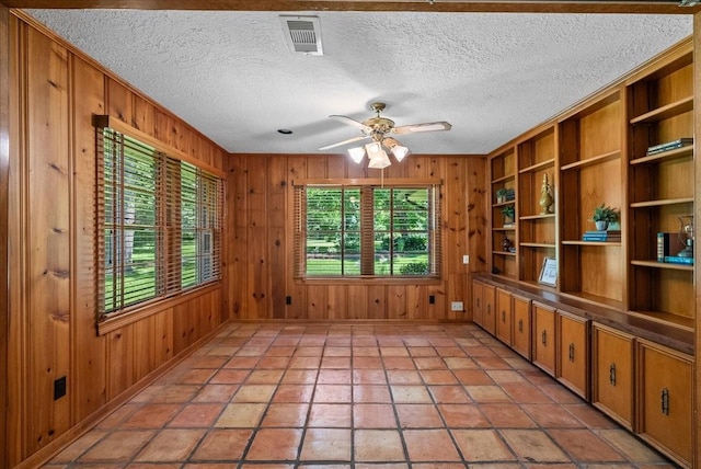 spare room with a textured ceiling, wood walls, plenty of natural light, and visible vents