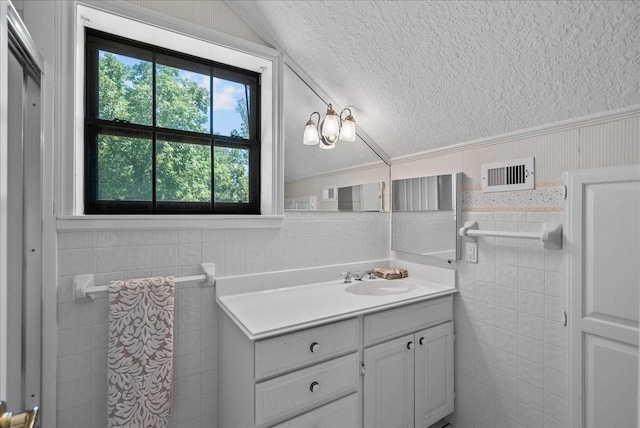 bathroom featuring a textured ceiling, a wainscoted wall, vanity, visible vents, and vaulted ceiling