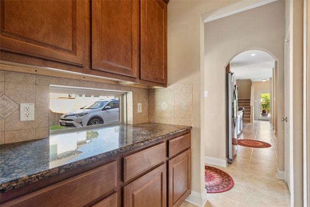 kitchen featuring stainless steel fridge, tasteful backsplash, light tile patterned floors, and dark stone countertops