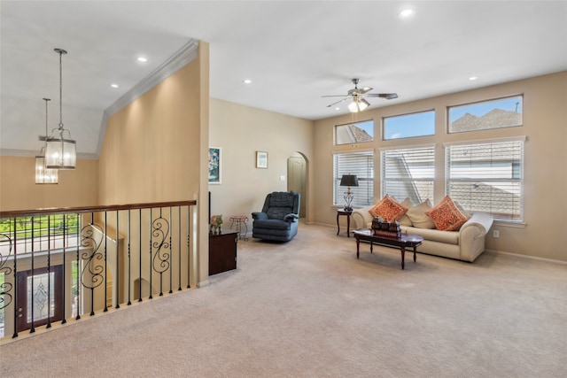 carpeted living room with ceiling fan with notable chandelier and crown molding