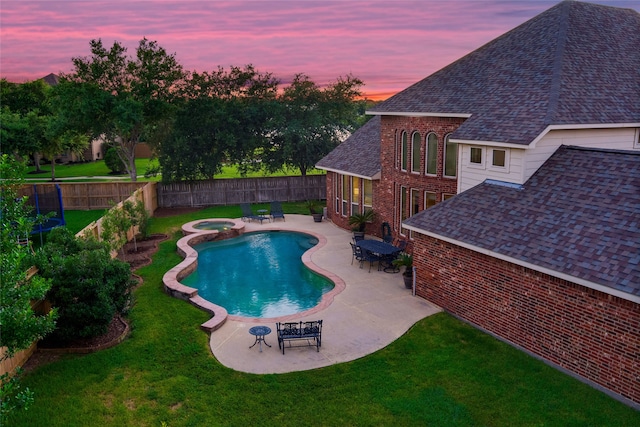 pool at dusk featuring an in ground hot tub, a yard, and a patio area