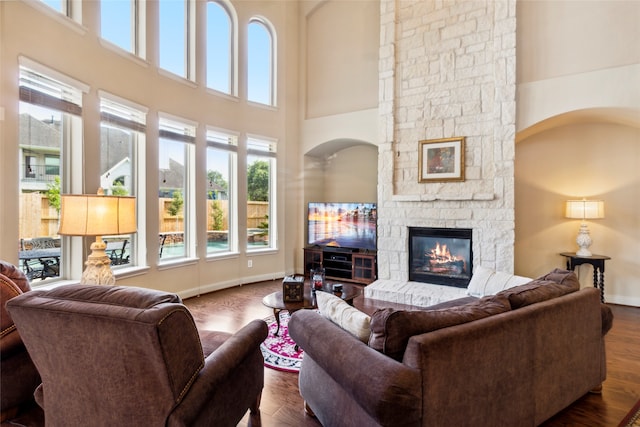 living room featuring a stone fireplace, a towering ceiling, and dark wood-type flooring