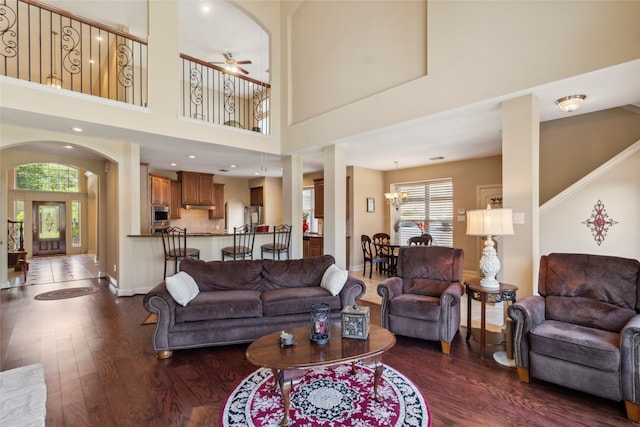 living room featuring dark hardwood / wood-style flooring, ceiling fan with notable chandelier, and a high ceiling