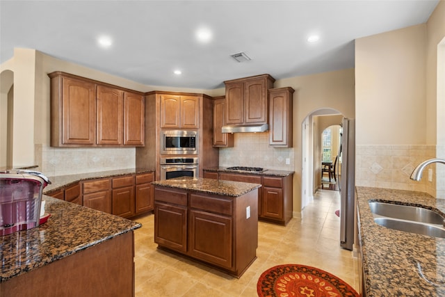 kitchen featuring sink, a center island, dark stone counters, and appliances with stainless steel finishes