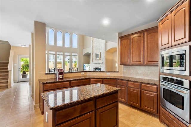 kitchen with decorative backsplash, light tile patterned floors, light stone counters, kitchen peninsula, and stainless steel appliances