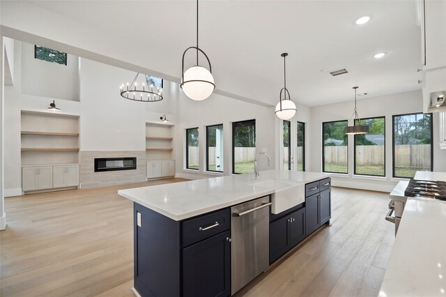 kitchen with pendant lighting, sink, a kitchen island with sink, light wood-type flooring, and stainless steel dishwasher