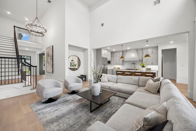 living room with a notable chandelier, stairs, light wood finished floors, and visible vents