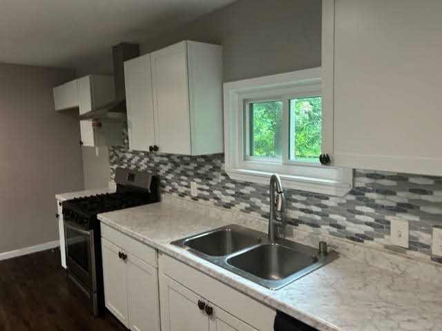 kitchen with dark hardwood / wood-style floors, stainless steel gas range oven, white cabinets, and backsplash