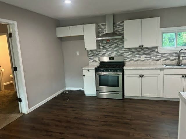 kitchen with stainless steel range with gas stovetop, sink, white cabinetry, and wall chimney exhaust hood