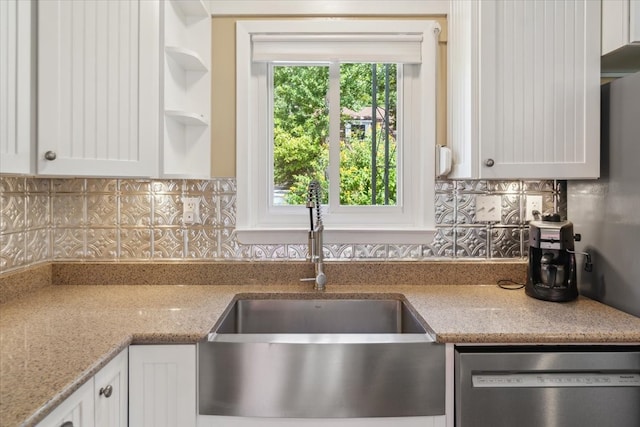 kitchen featuring stainless steel dishwasher, white cabinets, light stone counters, backsplash, and sink