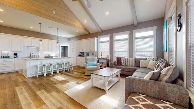 living room with beamed ceiling, light wood-type flooring, high vaulted ceiling, and sink