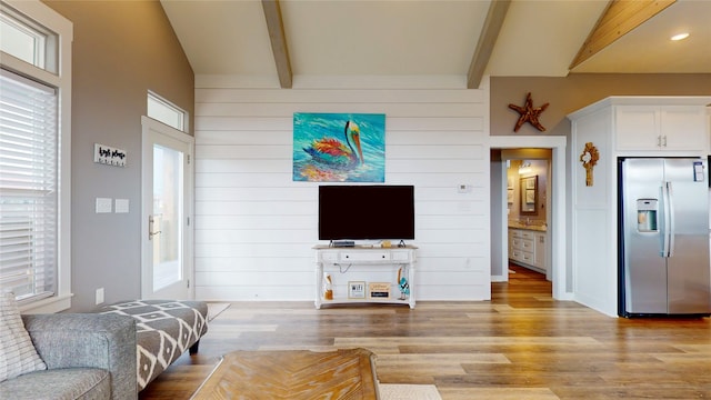 living room with lofted ceiling with beams, wood walls, and light wood-type flooring