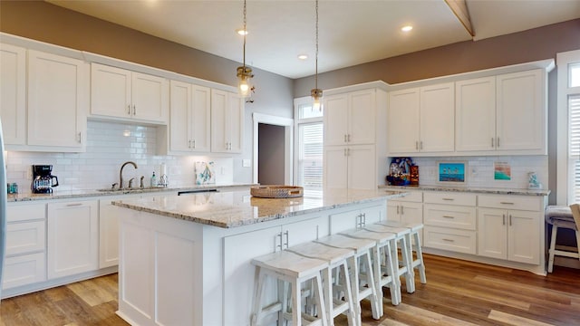 kitchen featuring backsplash, a kitchen island, sink, light hardwood / wood-style flooring, and white cabinetry