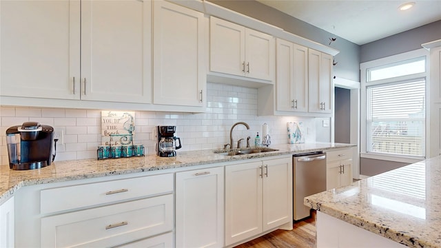 kitchen with dishwasher, white cabinetry, light stone countertops, and sink