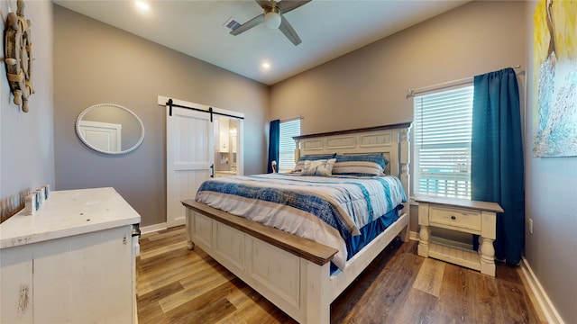 bedroom featuring connected bathroom, a barn door, ceiling fan, and wood-type flooring