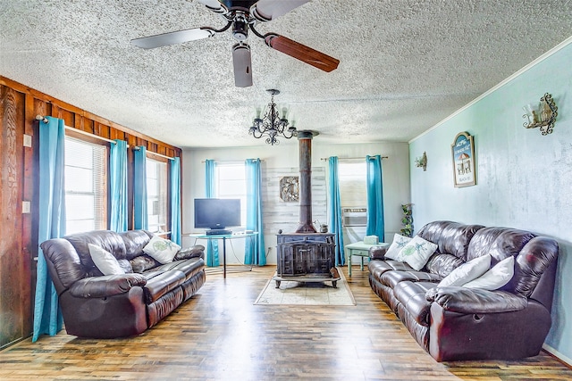 living room featuring a textured ceiling, ceiling fan with notable chandelier, hardwood / wood-style flooring, wood walls, and a wood stove