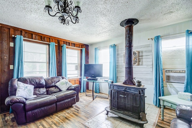 living room featuring a textured ceiling, wooden walls, hardwood / wood-style floors, a wood stove, and a chandelier