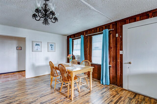 dining room featuring a notable chandelier, a textured ceiling, wood-type flooring, and wood walls