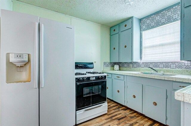 kitchen featuring white appliances, blue cabinetry, a textured ceiling, sink, and hardwood / wood-style flooring