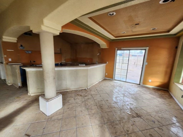 interior space with decorative columns, a tray ceiling, and light tile flooring