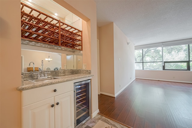 bar featuring dark hardwood / wood-style flooring, wine cooler, sink, light stone countertops, and a textured ceiling