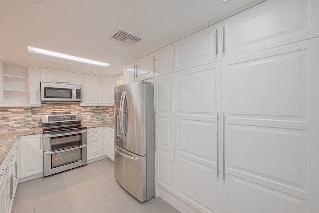 kitchen featuring stainless steel appliances, light stone countertops, decorative backsplash, and white cabinetry