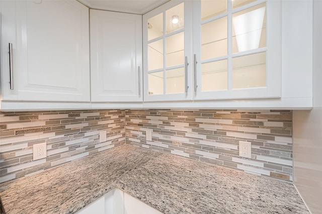 room details featuring glass insert cabinets, tasteful backsplash, light stone counters, and white cabinets