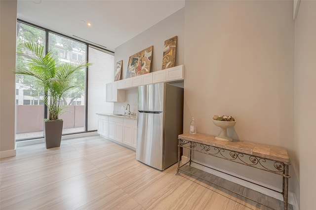 interior space with stainless steel refrigerator, white cabinets, sink, and floor to ceiling windows