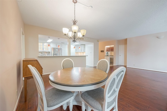 dining room with a chandelier, a textured ceiling, wine cooler, wood finished floors, and baseboards