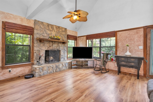 living room featuring a stone fireplace, light hardwood / wood-style flooring, high vaulted ceiling, and ceiling fan