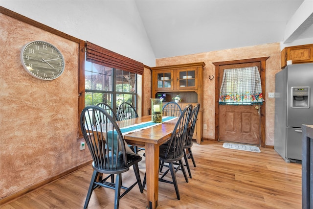 dining area with high vaulted ceiling and light hardwood / wood-style floors