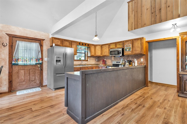 kitchen featuring light hardwood / wood-style flooring, kitchen peninsula, appliances with stainless steel finishes, pendant lighting, and vaulted ceiling