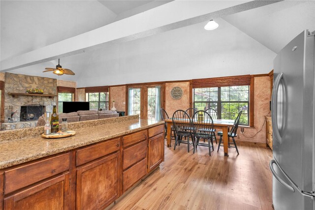 kitchen featuring lofted ceiling with beams, a fireplace, stainless steel refrigerator, light hardwood / wood-style floors, and ceiling fan