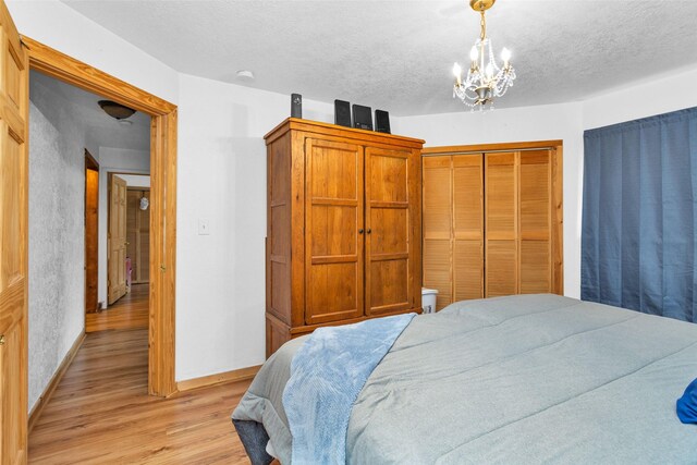 bedroom featuring a textured ceiling, light hardwood / wood-style flooring, a notable chandelier, and a closet