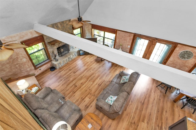 living room featuring high vaulted ceiling, light hardwood / wood-style flooring, ceiling fan, and a stone fireplace