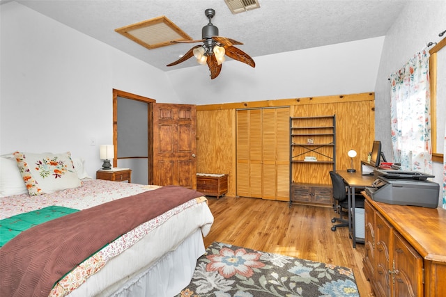 bedroom with a closet, vaulted ceiling, light wood-type flooring, a textured ceiling, and ceiling fan